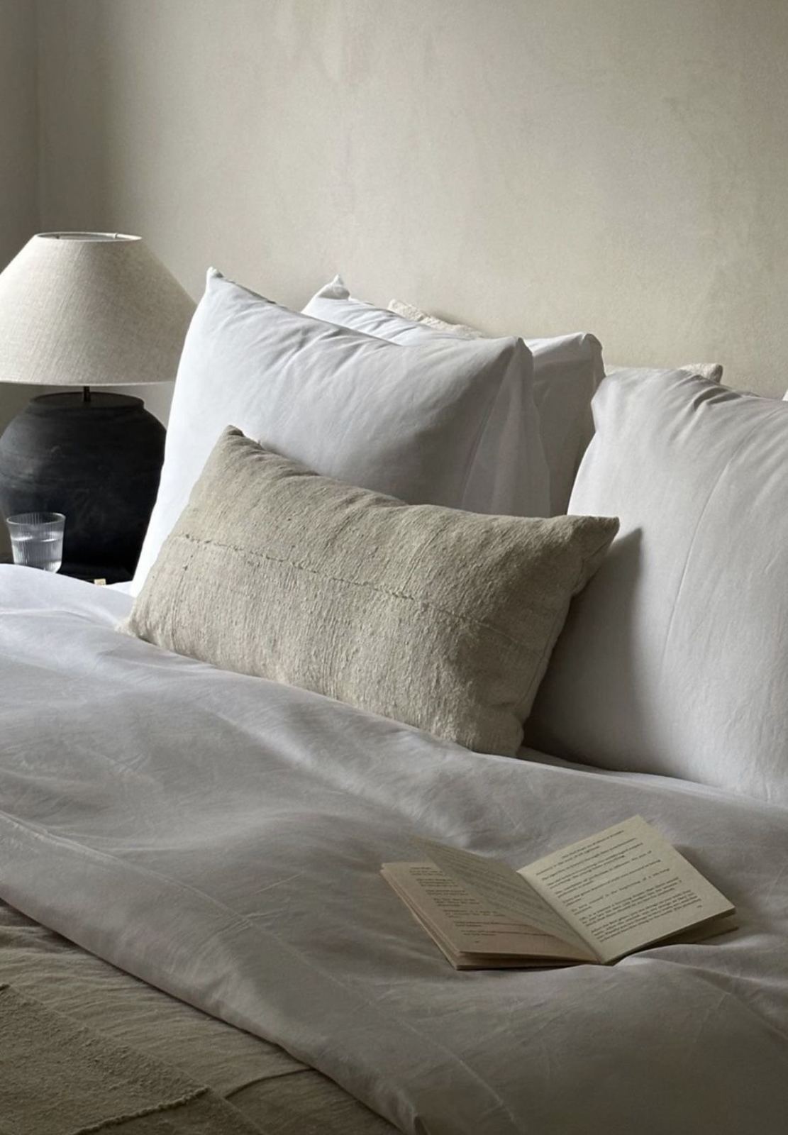 Cama vestida de blanco con cojín de lino y un libro abierto